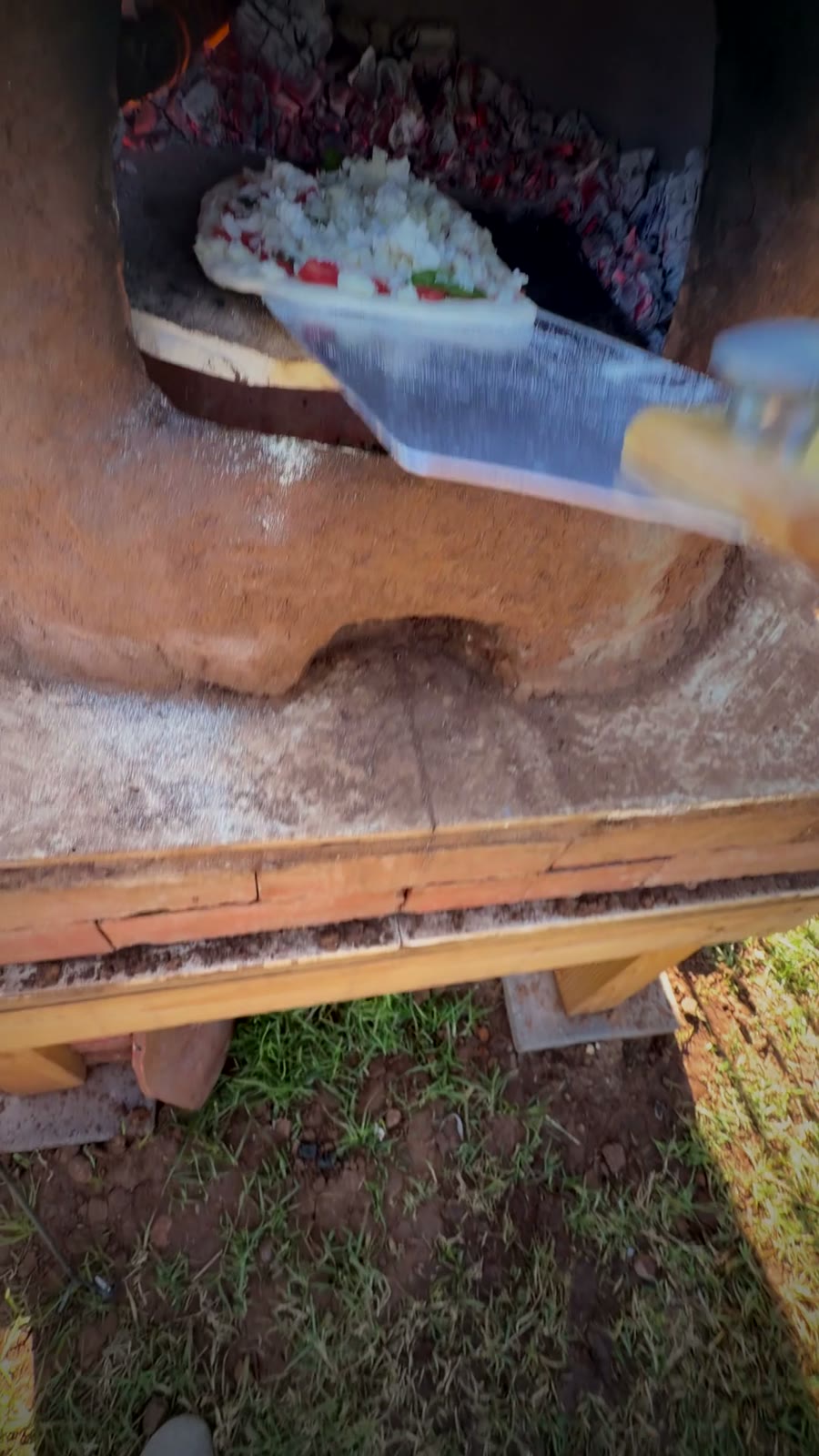 A topped pizza on a peel going into the wood-fired oven